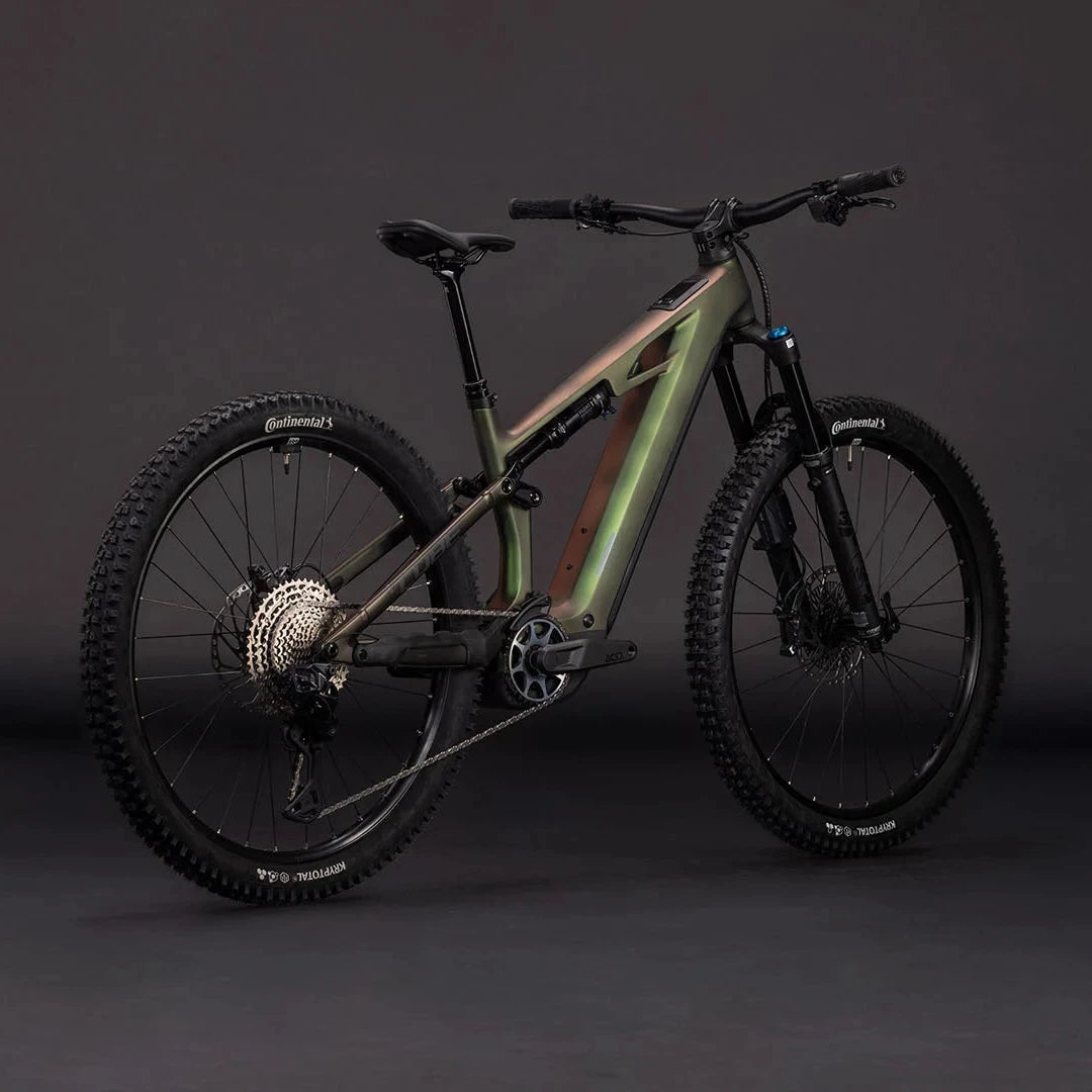A full-suspension electric mountain bike with a matte olive green frame, black components, and knobby tires, photographed in a studio setting against a dark gray background.
