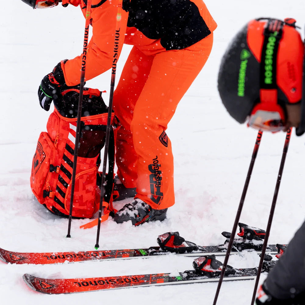 Person in orange ski suit preparing skis on a snowy surface