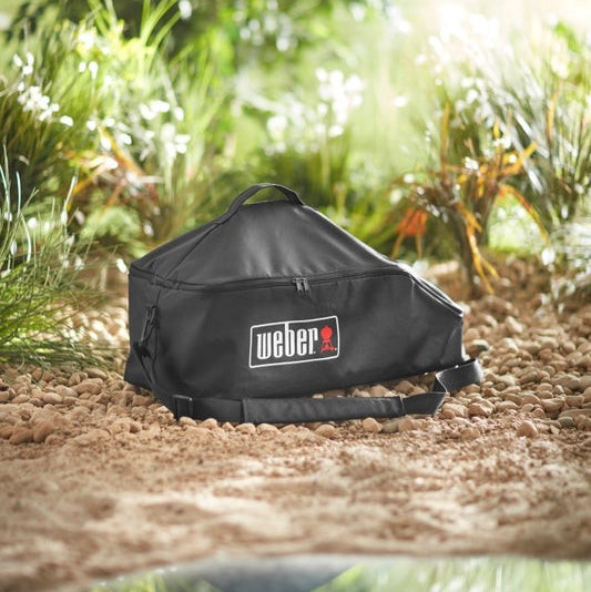 Black Weber grill cover on the ground with a natural background