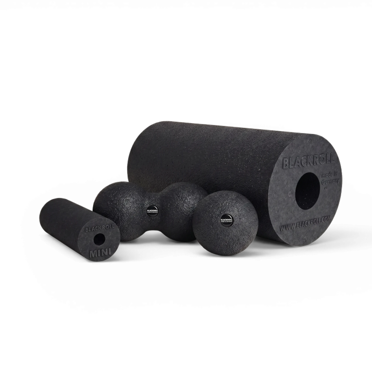 Black textured foam massage tools including a large cylindrical roller, a smaller cylindrical roller, and three spherical balls, arranged on a clean white background.