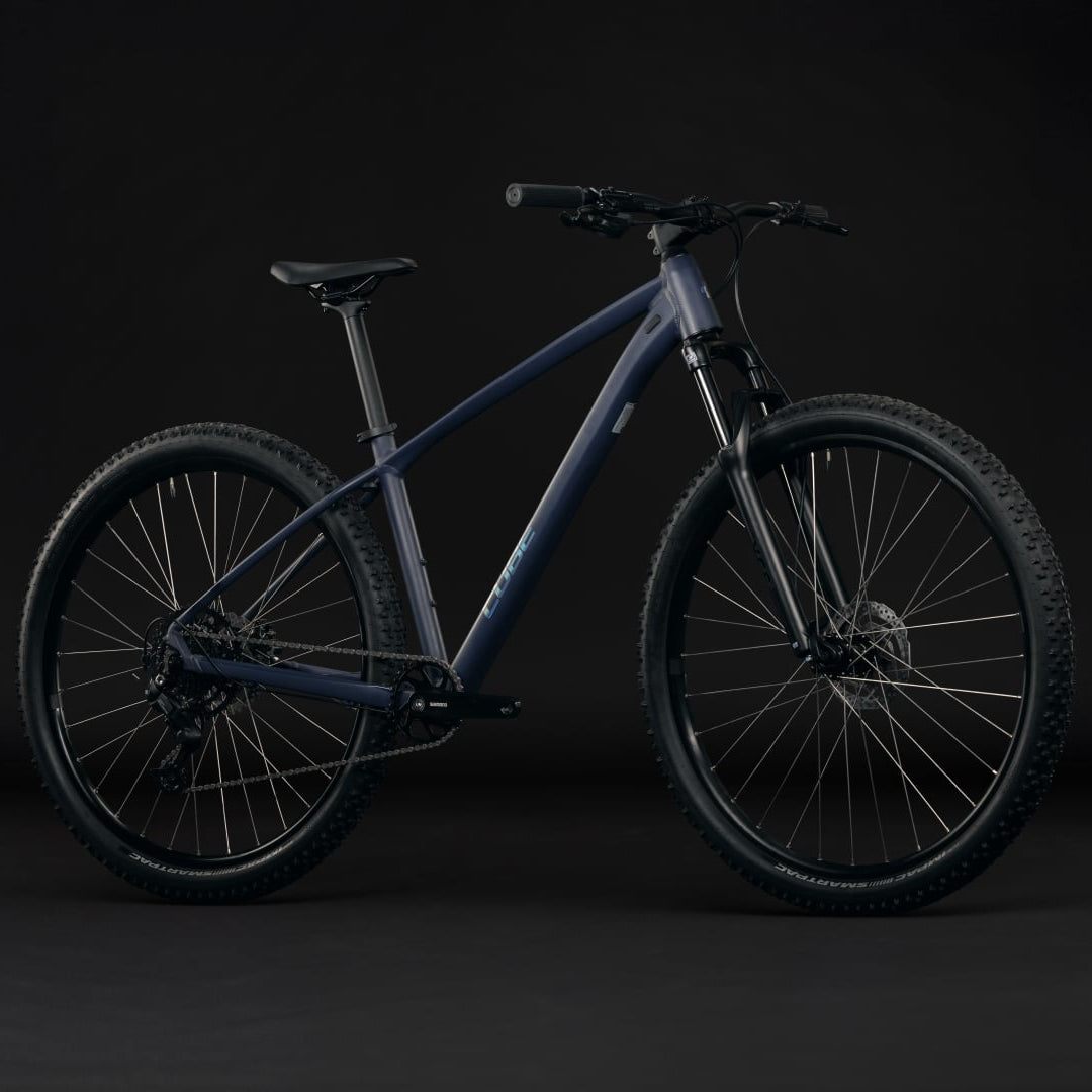 A dark mountain bike with a matte charcoal gray frame, black tires, and black components, photographed in a side profile against a dark studio background.