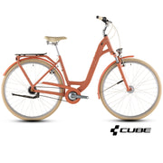 An orange step-through city bicycle with beige tires, a beige saddle, and silver components, shown from a side profile on a white background with a CUBE logo in the bottom right corner.