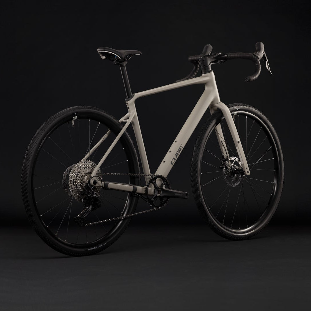 A modern drop-bar bicycle with a matte light gray frame and black components, photographed in a dark studio setting.