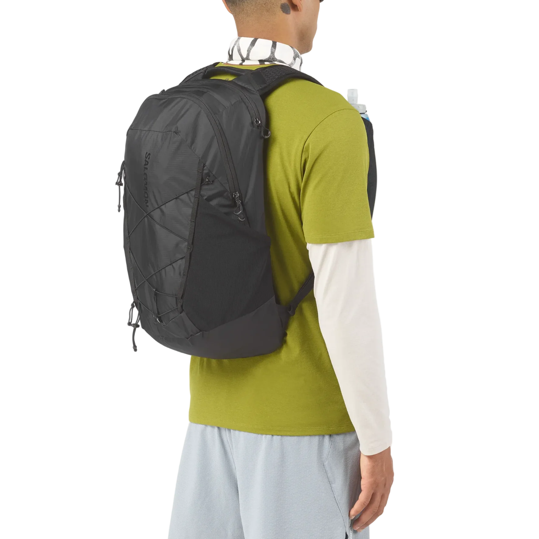 A man shown from the back wearing a black HOKS backpack, styled with a green and white long-sleeve shirt and light blue pants against a white background.