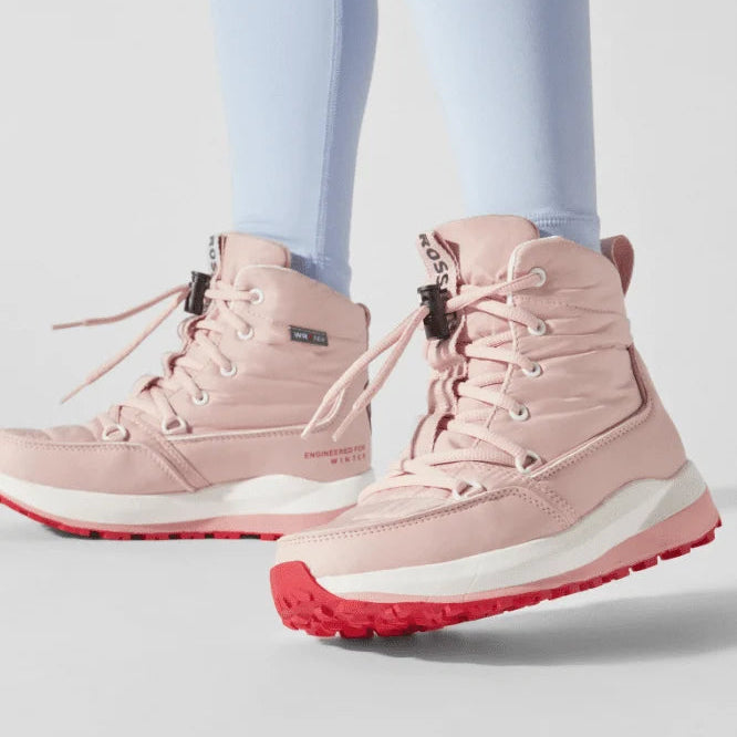 A pair of light pink mid-calf hiking boots with red soles, shown on a model wearing light blue leggings against a light gray studio background.