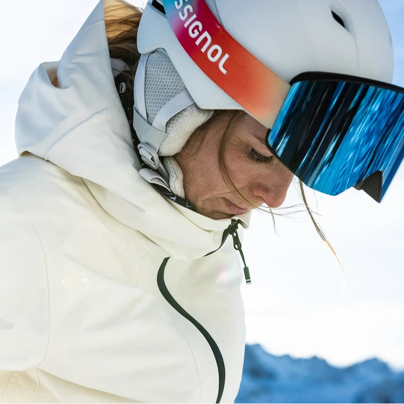 Rossignol ski goggles shown on a model in a snowy outdoor setting on the left, and a clean product rendering of the goggles on the right. The goggles feature a white helmet, blue mirrored lenses, and a strap with a red-to-purple gradient and the Rossignol logo.