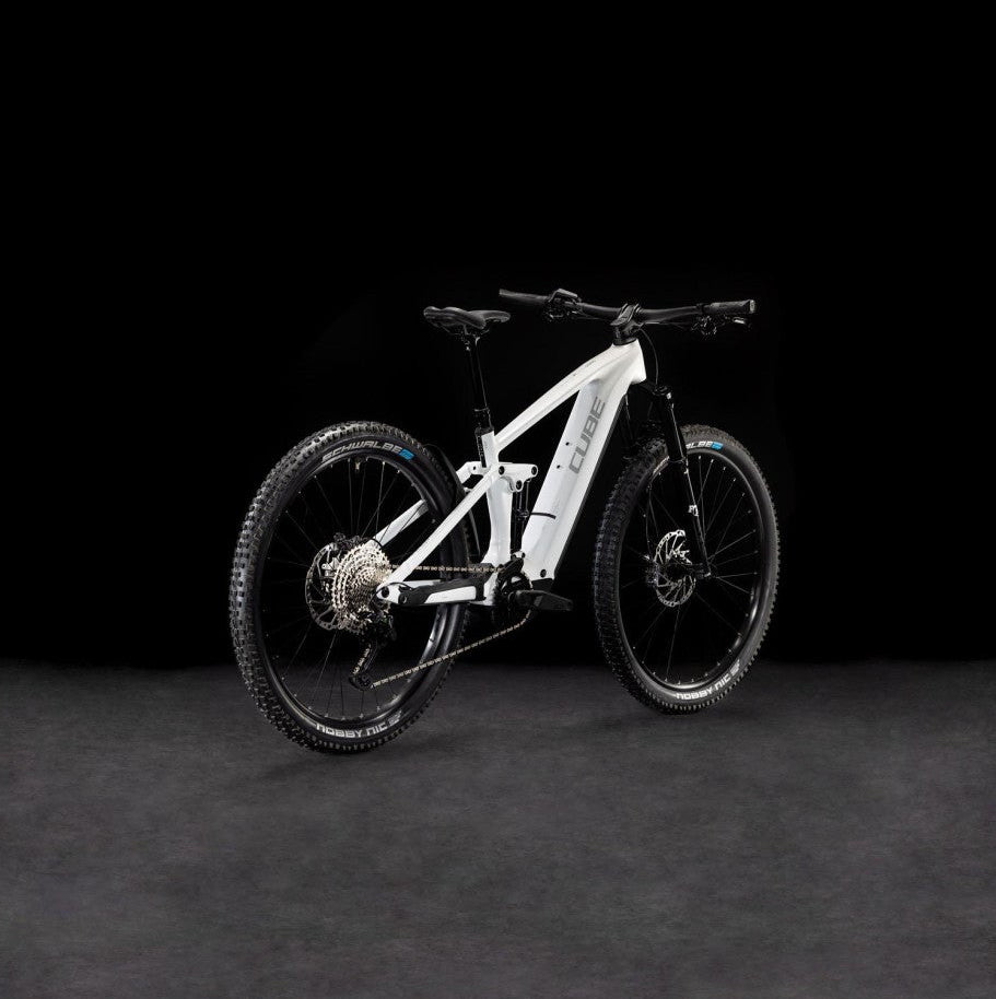 A white full-suspension electric mountain bike with black components, photographed in a studio setting against a dark black background and gray floor.