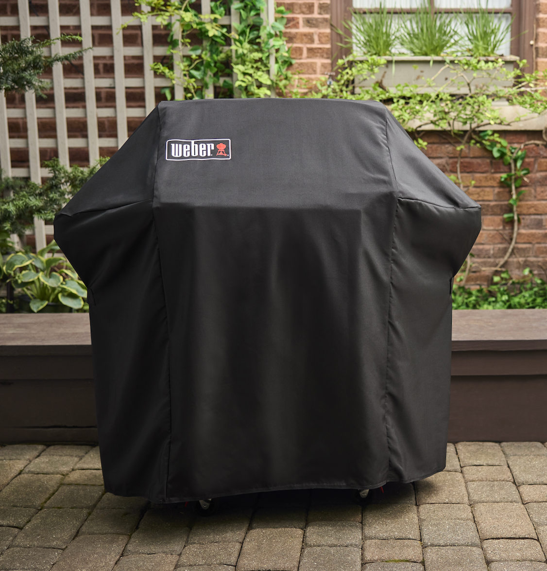 Black Weber grill cover on a grill outdoors with a garden background