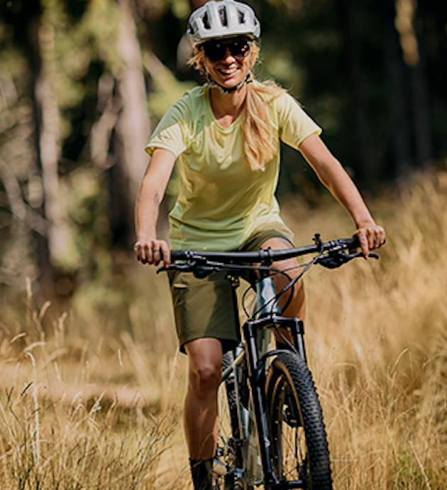 Woman riding mountain bike in forest wearing cycling helmet outdoor biking trail ride